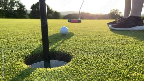 Missing the hole on a golf green. A young player putts the ball to hard and it goes flying out of the hole