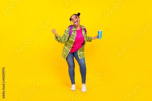 Full body photo of cheerful afro american woman wear backpack hold drink winner isolated on yellow color background