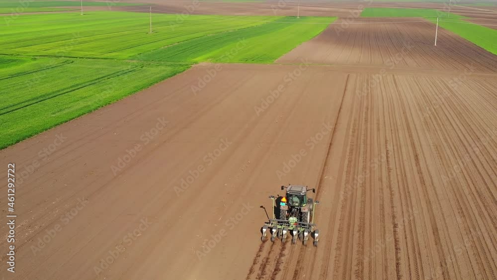 Aerial view of a farmer in tractor seeding and cultivating land, drone shot of sowing agricultural crops at field, around is a fields of green wheat in the spring season Aerial view of a farmer in tractor seeding and cultivating land, drone shot of sowing agricultural crops at field, around is a fields of green wheat in the spring season
