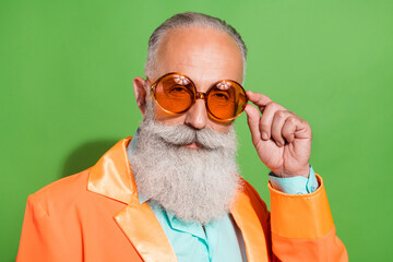 Portrait of attractive serious imposing groomed man touching specs isolated over vibrant green color background