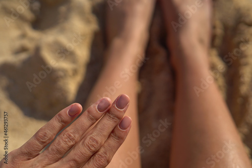 Nude brown natural summer manicure on the hands of a girl on the beach against a background of sand