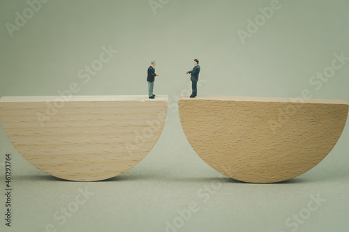 Miniature businessman stand on wood seesaw on endwise and shaking hands. Business, management photo
