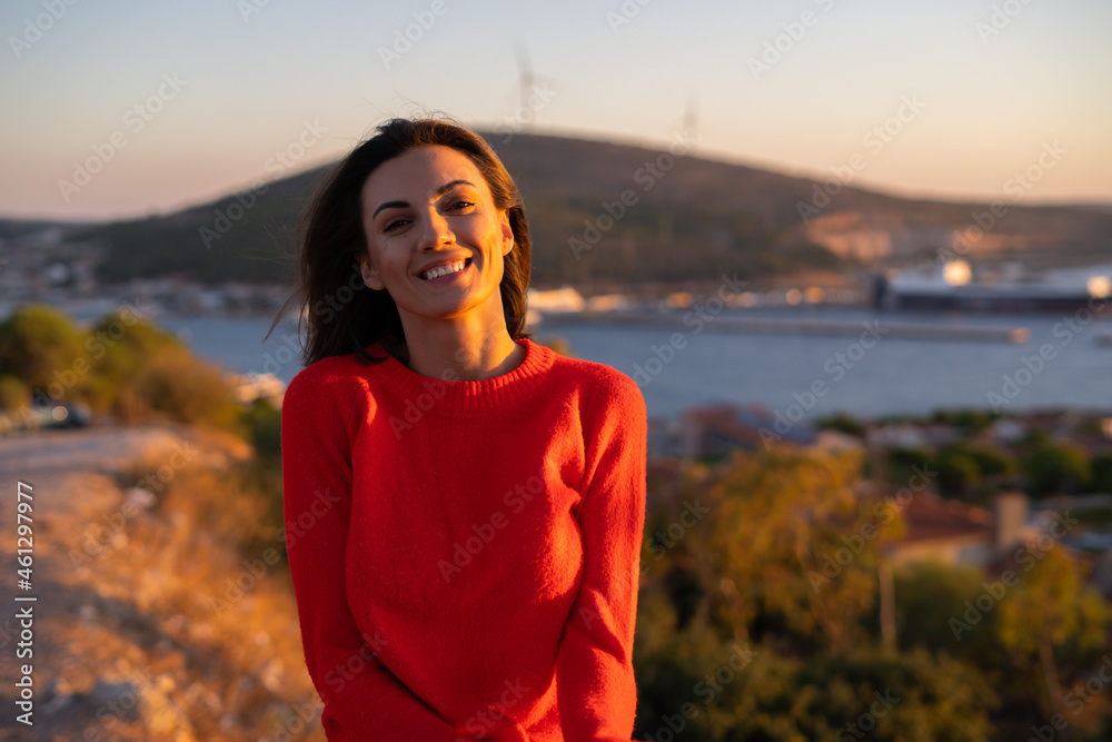 Young woman in a red sweater at a magnificent sunset on the mountain against the background of the sea, romantic mood, smiling happily Young woman in a red sweater at a magnificent sunset on the mountain against the background of the sea, romantic mood, smiling happily