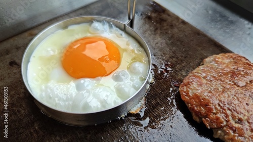 Fried egg in stainless steel mold ring and fried cutlet on hot pan.