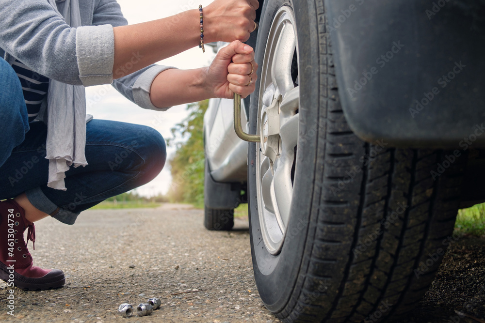 Changing wheel, woman hands unscrewing bolts on flat car tire on the road.