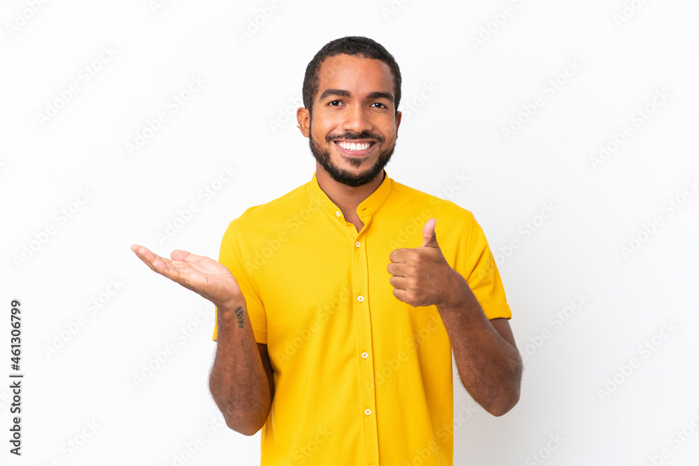 Young Ecuadorian man isolated on white background holding copyspace imaginary on the palm to insert an ad and with thumbs up Young Ecuadorian man isolated on white background holding copyspace imaginary on the palm to insert an ad and with thumbs up