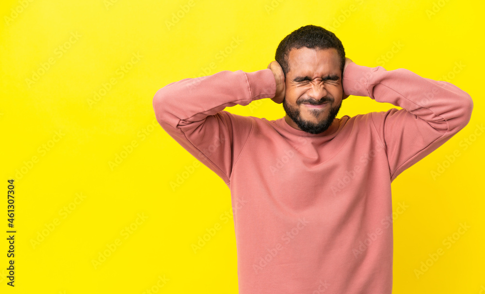 Young latin man isolated on yellow background frustrated and covering ears Young latin man isolated on yellow background frustrated and covering ears