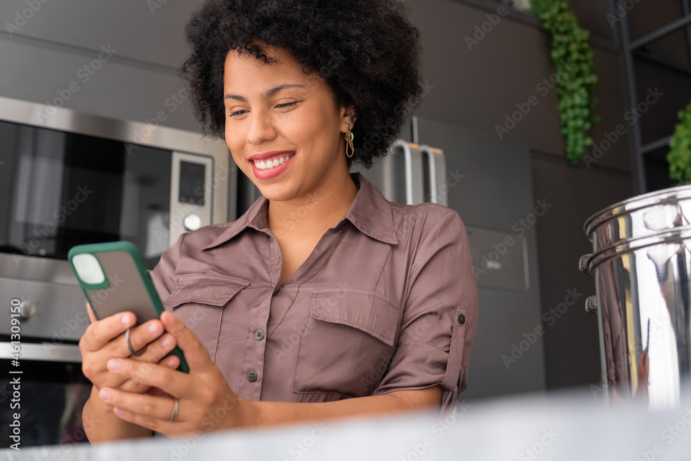 brazilian woman looking at mobile and smiling in kitchen counter brazilian woman looking at mobile and smiling in kitchen counter
