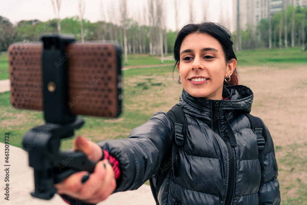 Beautiful Latina influencer recording content for her vlog in a plaza on a very cloudy day. Millennial concept. communication, content for networks.