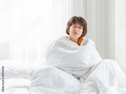 Sleepy woman is sitting in bed, completely covered with white blanket. It's hard to wake up early in morning. © Konstantin Aksenov