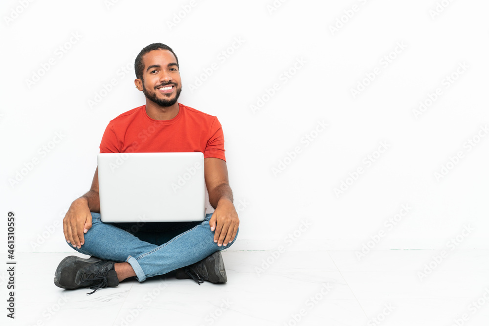 Young Ecuadorian man with a laptop sitting on the floor isolated on white background with arms crossed and looking forward Young Ecuadorian man with a laptop sitting on the floor isolated on white background with arms crossed and looking forward