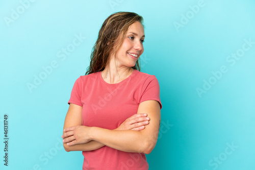Young caucasian woman isolated on blue background with arms crossed and happy