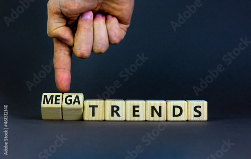 Trends or megatrends symbol. Businessman turns cubes and changes words trends to megatrends. Beautiful grey table, grey background, copy space. Business and trends or megatrends concept.