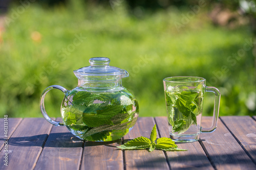Healthy nettle tea in a glass tea pot and mug in the summer garden on wooden table