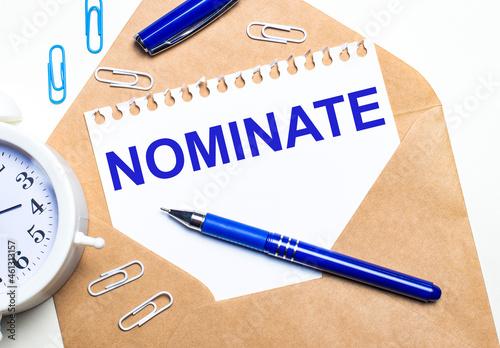 On a light background, a craft envelope, an alarm clock, paper clips, a blue pen and a sheet of paper with the text NOMINATE photo