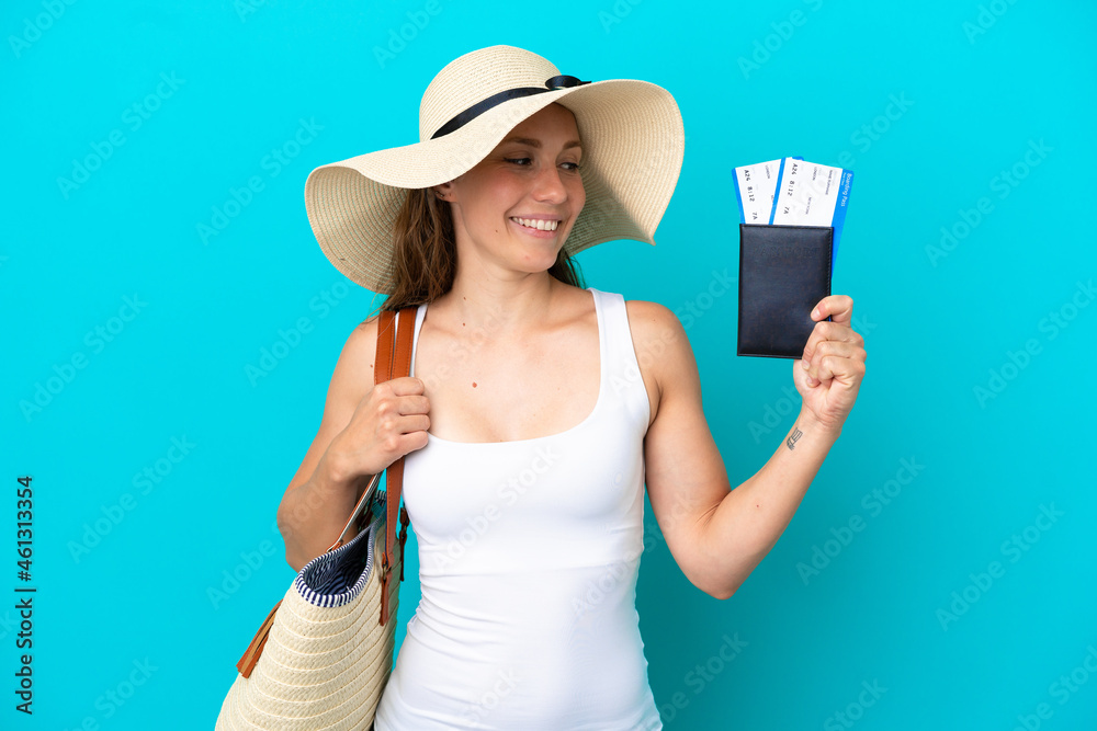 Young caucasian woman holding a beach bag and passport with pamel isolated on blue background with happy expression Young caucasian woman holding a beach bag and passport with pamel isolated on blue background with happy expression