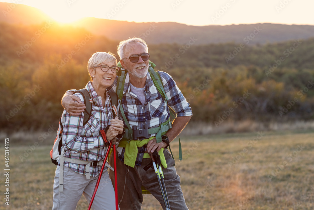 Obraz premium Couple of mature people smile and rest afther walking in nature with sunset on background
