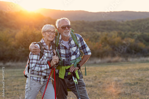 Couple of mature people smile and rest afther walking in nature with sunset on background