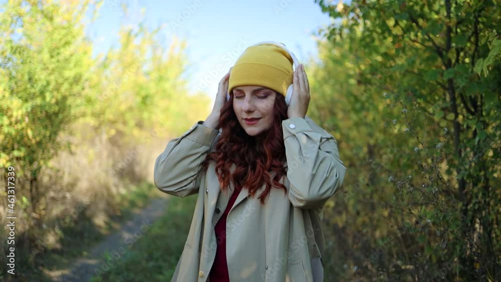 Caucasian joyful beautiful young woman putting on wireless headphones outside at a autumn park. Technology and happiness concept. Caucasian joyful beautiful young woman putting on wireless headphones outside at a autumn park. Technology and happiness concept.