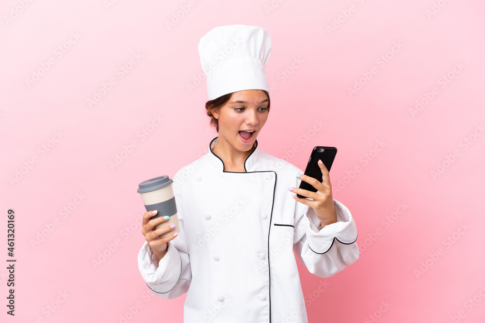 Little caucasian chef girl isolated on pink background holding coffee to take away and a mobile Little caucasian chef girl isolated on pink background holding coffee to take away and a mobile