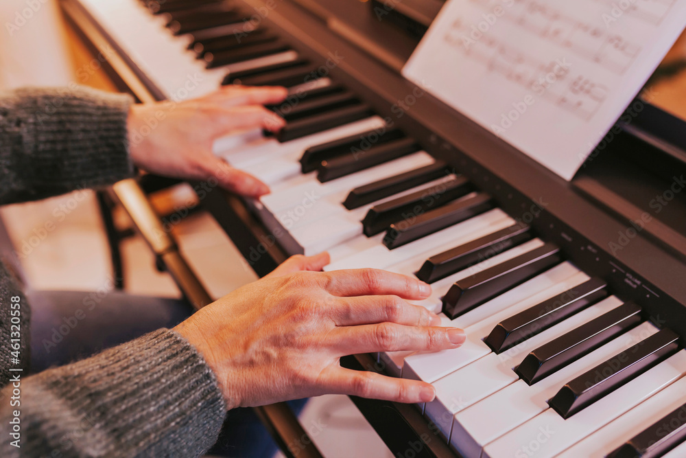 Obraz premium Close-up of girl hands on the piano, woman playing the piano. Christmas lights and music, concert, family time, holidays concept. Merry Christmas, happy new year.