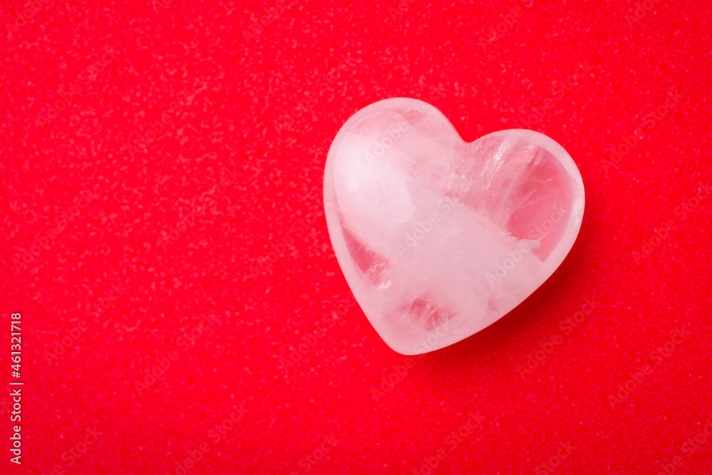 Fototapeta premium White transparent stone in shape of heart on red table. Valentine`s day background