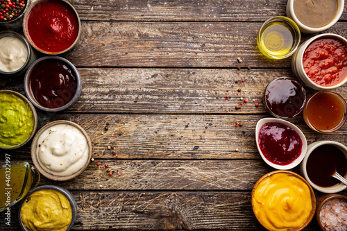 Set of different bowls of various dip sauces on wooden background, top view photo