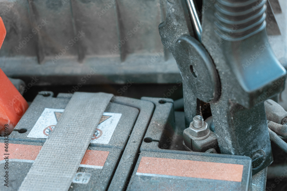 Close-up with selective focus of starter clamps hooked to the terminals of a dusty old car battery Close-up with selective focus of starter clamps hooked to the terminals of a dusty old car battery