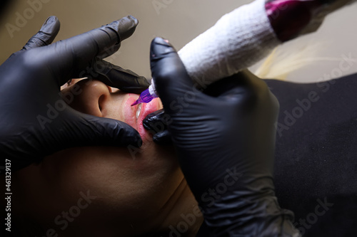 the tattoo artist stretches the upper lip of the model and performs the tattoo