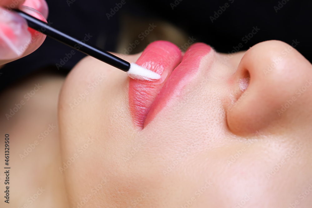 the tattoo artist distributes a drop of oil on the lips of the model with a small brush the tattoo artist distributes a drop of oil on the lips of the model with a small brush