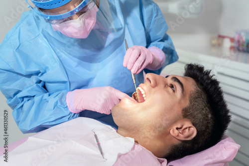 Young man having teeth examination at dentist office. Professional oral checkup in dentistry. Close up of female dentist working with dental tools in opened patient mouth. Stomatology and teeth care