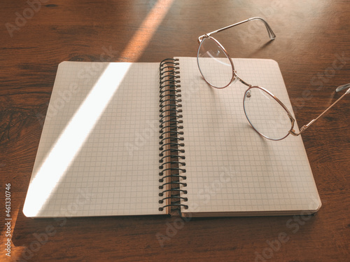 stylish glasses left on a notebook. The sun's rays create a beautiful shadow on the desktop. good morning at work. Blank notebook sheets