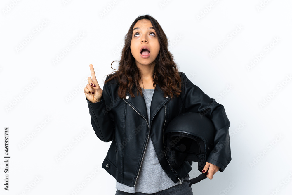 Young woman holding a motorcycle helmet over isolated white background pointing up and surprised Young woman holding a motorcycle helmet over isolated white background pointing up and surprised