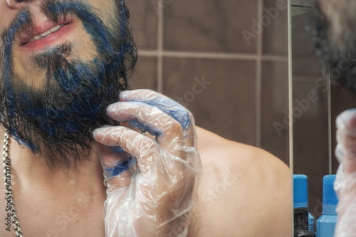 A mustachioed man with a beard is trying to dye his beard blue