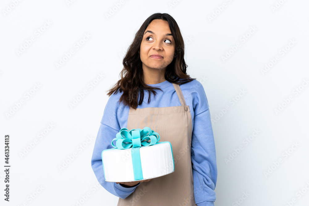 Pastry chef holding a big cake over isolated white background having doubts while looking up Pastry chef holding a big cake over isolated white background having doubts while looking up