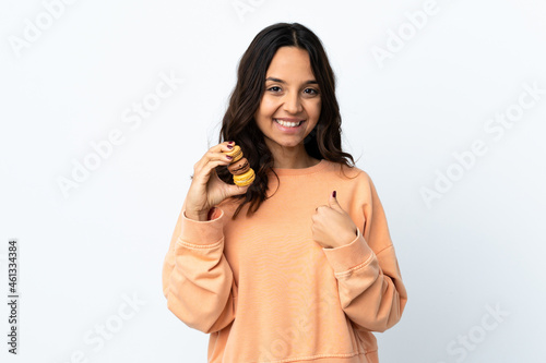 Young woman over isolated white background holding colorful French macarons with surprise expression
