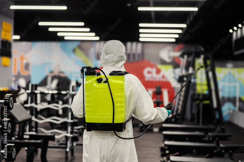 Stay healthy, warning for COVID 19. Professional in a protective uniform prevents the spread of the infection on a high-risk spot in the gym. Coronavirus pandemic, antiseptic, disinfection