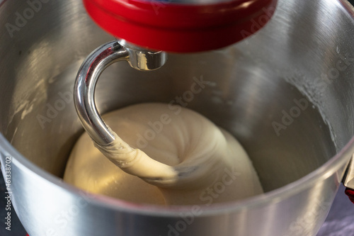Making pizza dough with machine in a steel bowl.