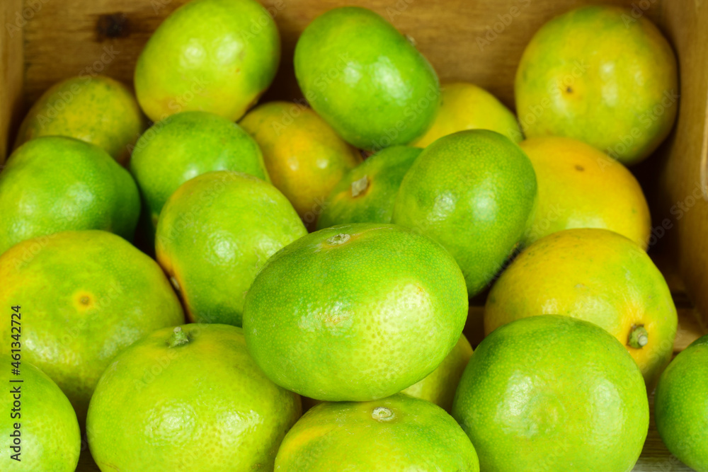 Close up, tangerine with green skin, more units behind in a group, next to a lying wooden box. Close up, tangerine with green skin, more units behind in a group, next to a lying wooden box.