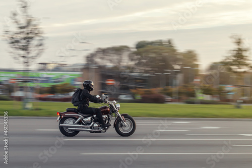 A motorcycle rides on the street at high speed in front of the rising sun. The motorcyclist dressed in all black. Motion blur