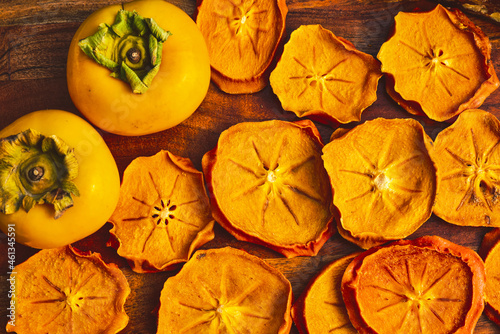 fresh whole ripe Japanese persimmons and dried fruit slices of persimmon on wood board autumn colors