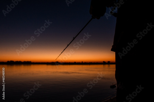 Detail shot of a man holding a fishing rod with the sunset in the background.