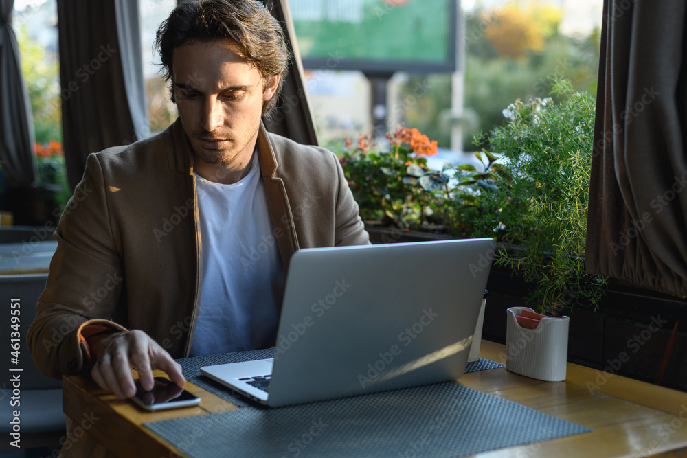 Good looking man using smartphone near laptop on terrace of cafe in evening Good looking man using smartphone near laptop on terrace of cafe in evening