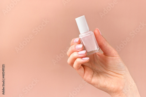 Female hand holding a pink nail polish bottle on a soft beige background. Natural manicure presentation. Luxury woman's cosmetics concept