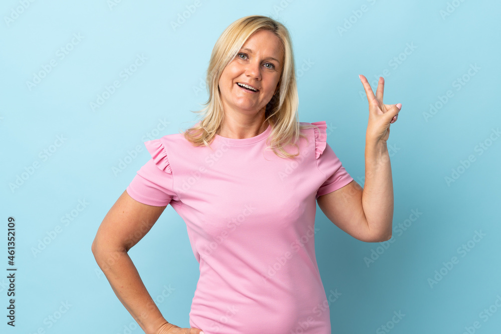 Fototapeta premium Middle age woman isolated on blue background smiling and showing victory sign
