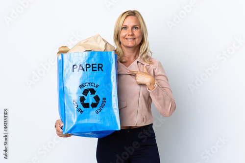 Middle age woman holding a recycling bag full of paper to recycle isolated on white background with surprise facial expression