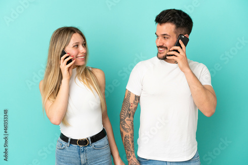 Young couple over isolated blue background talking to mobile