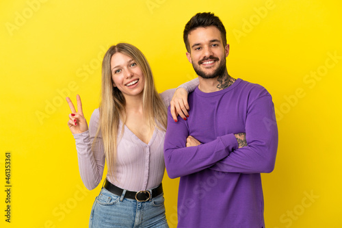 Young couple over isolated yellow background smiling and showing victory sign
