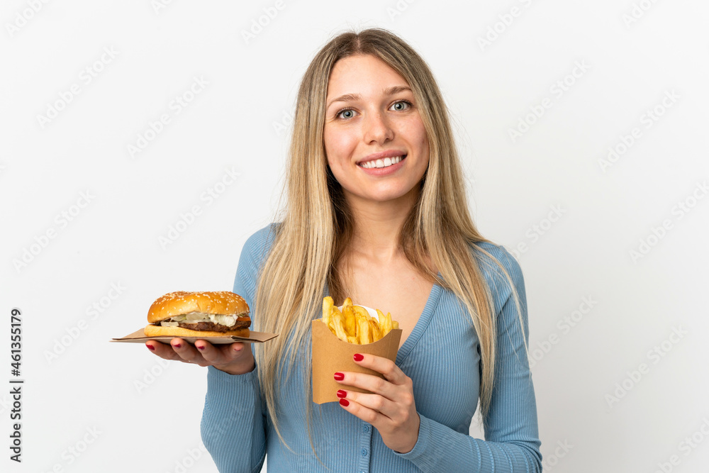 Young blonde woman holding fried chips and cheeseburger over isolated background Young blonde woman holding fried chips and cheeseburger over isolated background