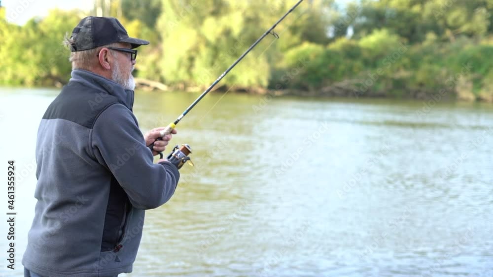 Mature gray-bearded man with glasses fisherman holding reel rod, spinning or spoon-bait and fishing on good summer day. Mens hobby